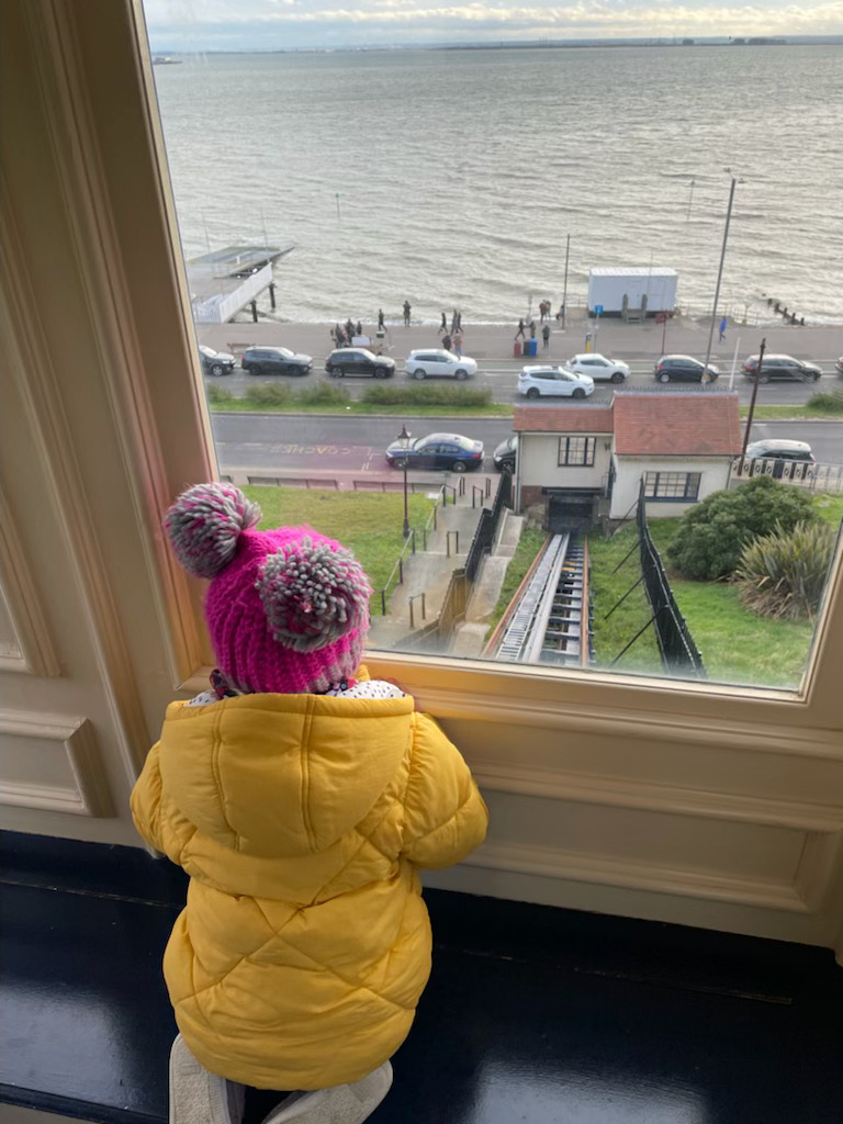 Looking down the tracks on the Southend Cliff Lift. In the foreground you an see the rear of a two year old wearing a yellow coat and pink bobble hat who is looking out of the window.