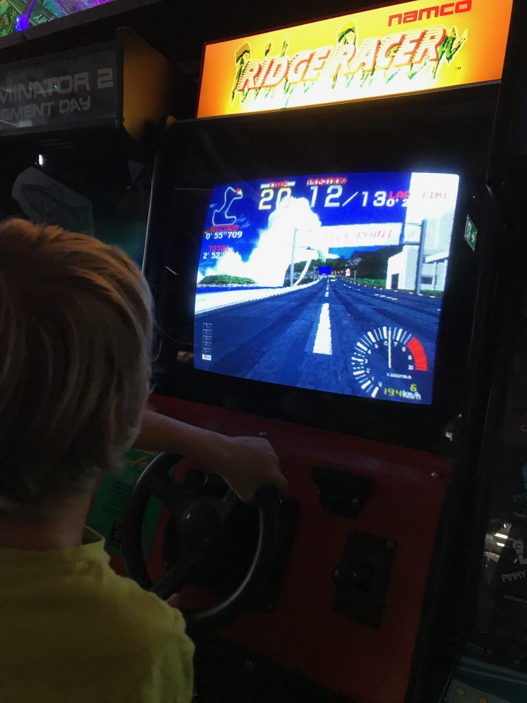 The back of teh head of a nine year old boy whilst he playing an arcade driving game.