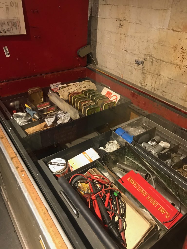 A picture of the top of an old Mail Rail carriage that was converted into an engineers trolly by someone who worked there. You can see an assortment of bits and bobs including a tin of swarfega, leads for a multimeter and an array of old tobacco tins