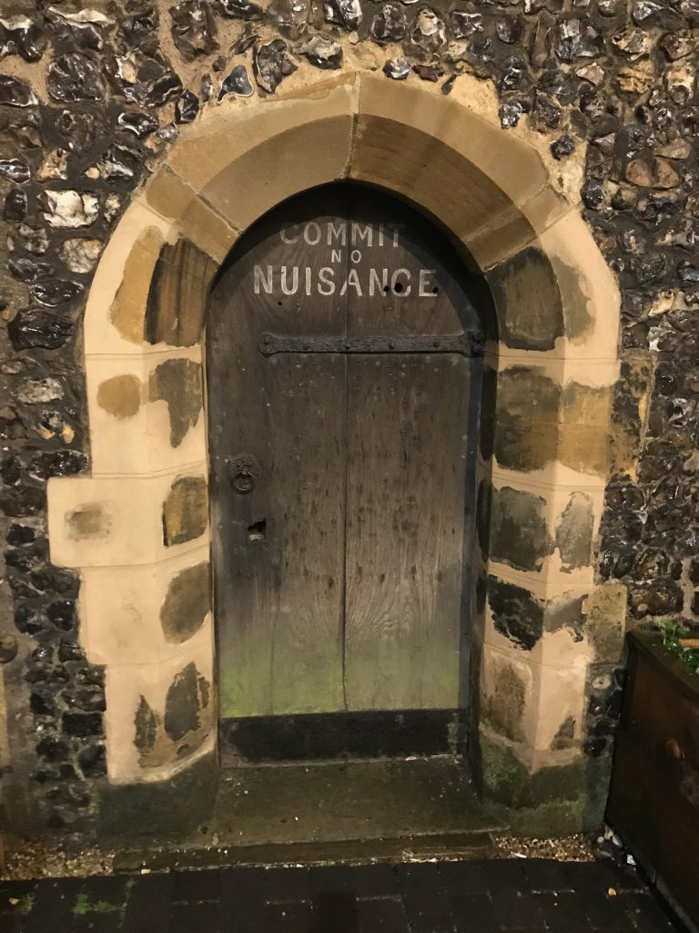 A wooden door set into the stone and flint tower with the words "Commit no nuisance" written on them at the top neatly in white paint.