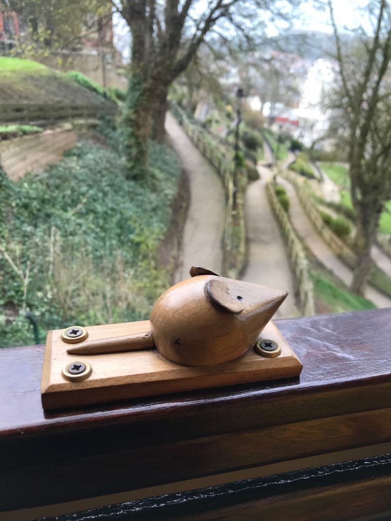 A carved wooden mouse sitting on a plaque on the window sill own a moving tramcar.